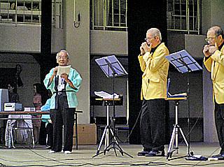 ハーモニカ演奏で「さざんかの宿」を歌う野村元代表